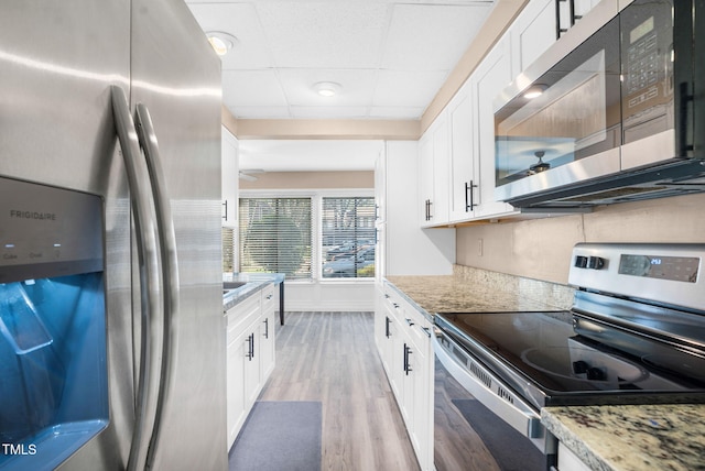 kitchen with ceiling fan, a paneled ceiling, white cabinets, appliances with stainless steel finishes, and light wood finished floors