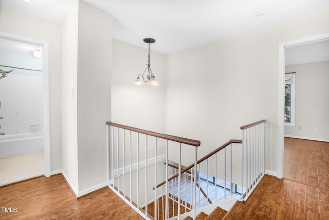 corridor featuring a notable chandelier, wood finished floors, an upstairs landing, and baseboards