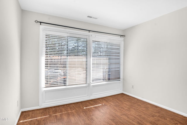 spare room featuring a healthy amount of sunlight, visible vents, baseboards, and wood finished floors