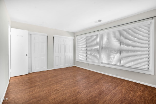 unfurnished bedroom with baseboards, wood finished floors, visible vents, and multiple closets