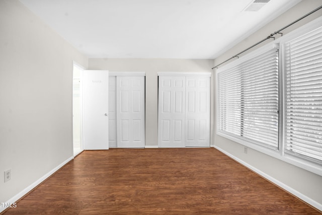 unfurnished bedroom with wood finished floors, visible vents, baseboards, and two closets