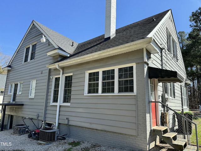 view of side of home with a chimney, cooling unit, and roof with shingles