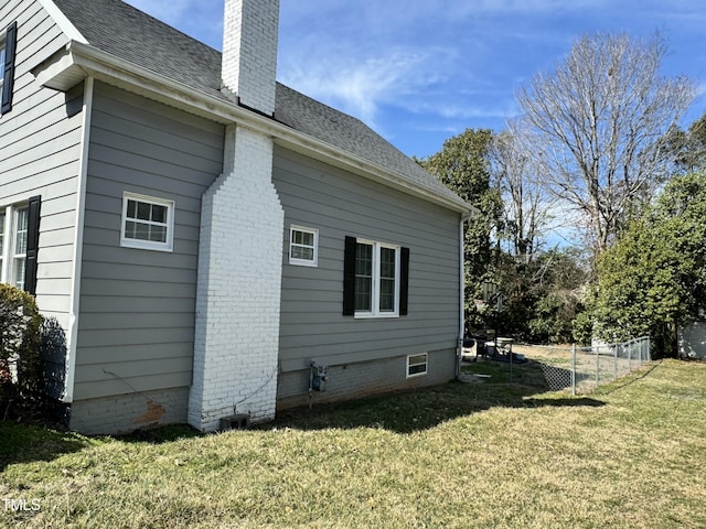 view of side of home featuring roof with shingles, a lawn, a chimney, and fence