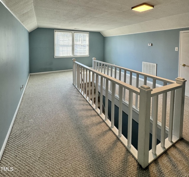 hallway featuring baseboards, lofted ceiling, a textured ceiling, an upstairs landing, and carpet floors