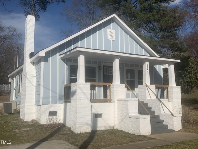 view of front facade featuring a porch, crawl space, cooling unit, and brick siding