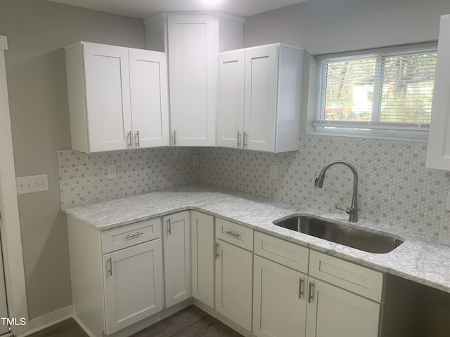 kitchen with backsplash, a sink, white cabinetry, and light stone countertops