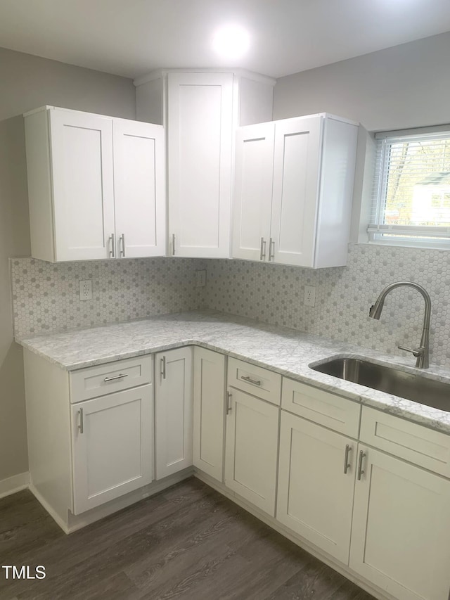 kitchen featuring tasteful backsplash, dark wood-style floors, light stone countertops, white cabinetry, and a sink