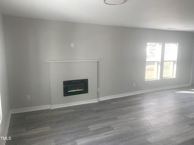 unfurnished living room featuring a glass covered fireplace, wood finished floors, and baseboards