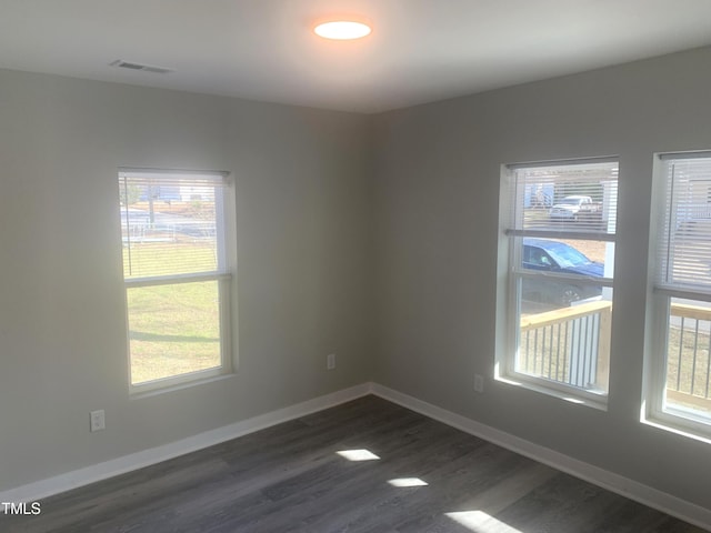 spare room featuring dark wood-style floors, baseboards, visible vents, and a wealth of natural light