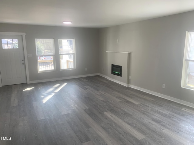 unfurnished living room with dark wood-style floors, a glass covered fireplace, and baseboards