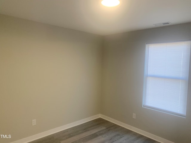 spare room with dark wood finished floors, visible vents, and baseboards