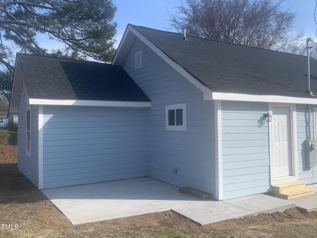 view of side of home with entry steps, a shingled roof, and a patio area