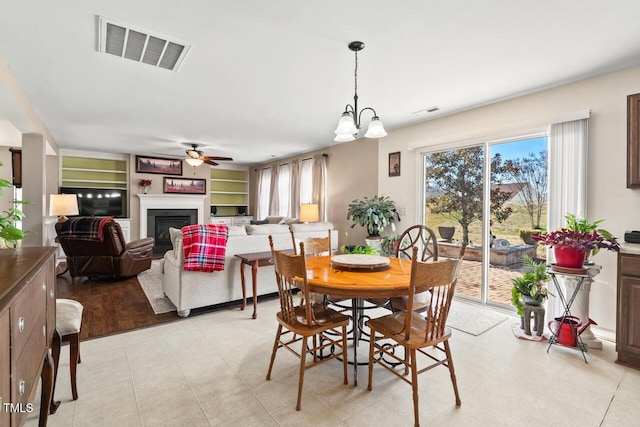 dining space with a healthy amount of sunlight, ceiling fan with notable chandelier, visible vents, and a glass covered fireplace