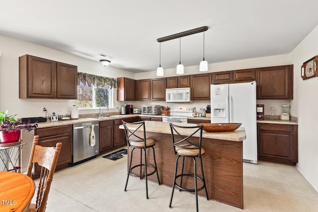 kitchen featuring white appliances, a kitchen island, a breakfast bar, light countertops, and a sink