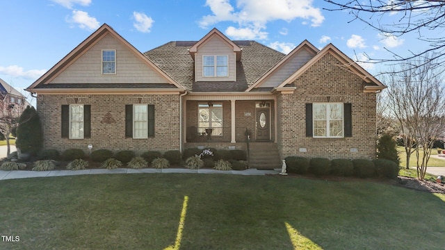 craftsman-style home with a porch, a front yard, brick siding, and roof with shingles