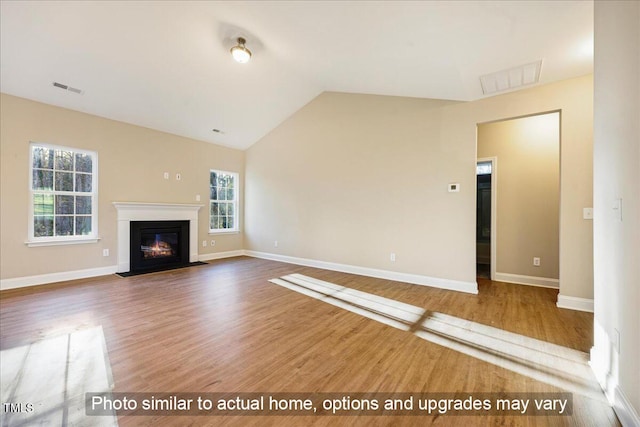 unfurnished living room with lofted ceiling, a fireplace with flush hearth, wood finished floors, baseboards, and visible vents