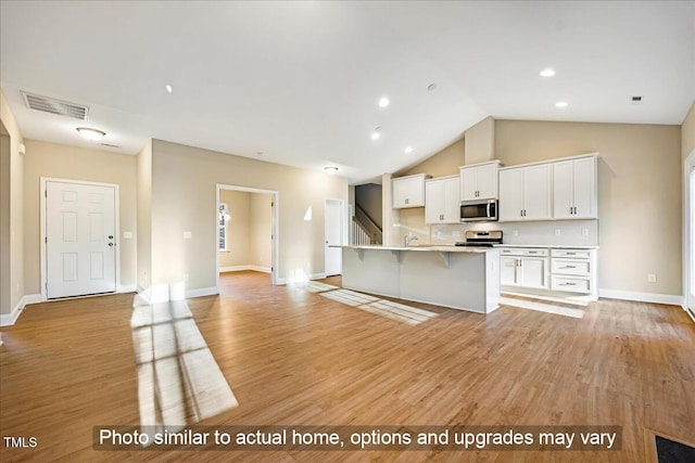 kitchen featuring stainless steel appliances, visible vents, a kitchen breakfast bar, white cabinetry, and light countertops