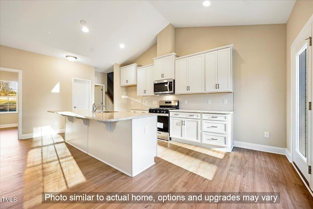 kitchen featuring light wood-style flooring, appliances with stainless steel finishes, white cabinets, a sink, and a kitchen bar