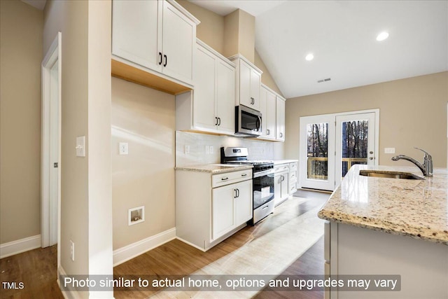 kitchen with tasteful backsplash, lofted ceiling, appliances with stainless steel finishes, a sink, and light stone countertops