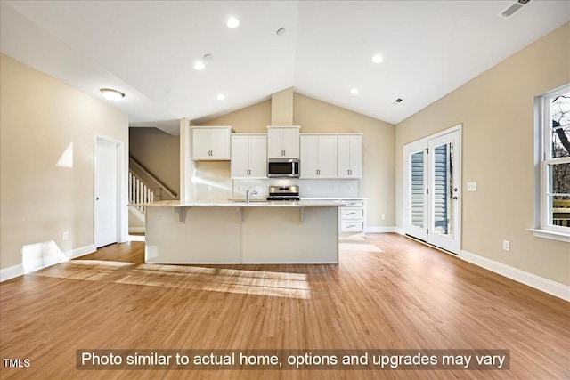 kitchen featuring visible vents, a breakfast bar, stainless steel appliances, white cabinetry, and a sink