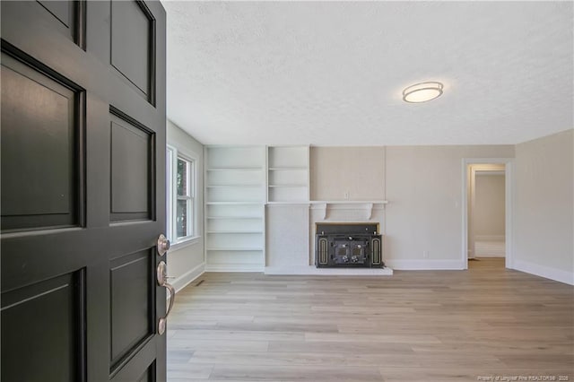 unfurnished living room with built in features, baseboards, a textured ceiling, and light wood finished floors