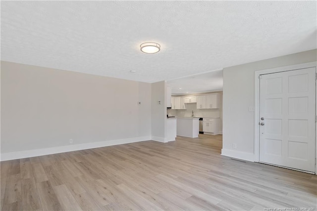 unfurnished living room with a textured ceiling, light wood finished floors, visible vents, and baseboards