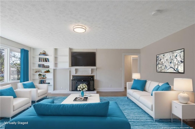 living room with built in shelves, baseboards, a textured ceiling, and wood finished floors