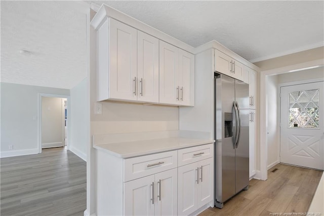 kitchen featuring a textured ceiling, white cabinets, light countertops, stainless steel refrigerator with ice dispenser, and light wood finished floors