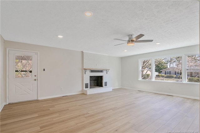 unfurnished living room featuring baseboards, light wood-style flooring, ceiling fan, a textured ceiling, and a fireplace