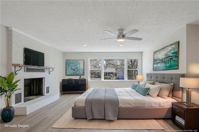 bedroom featuring a textured ceiling, ceiling fan, a fireplace, wood finished floors, and visible vents