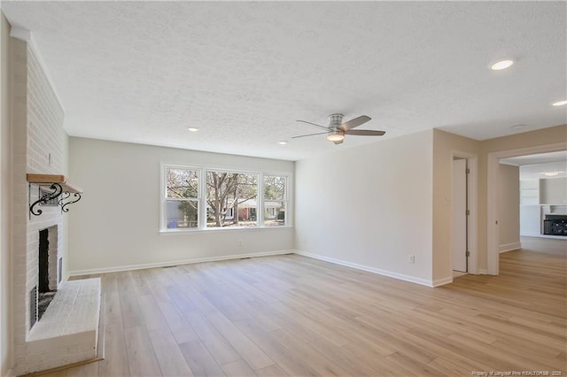 unfurnished living room featuring a brick fireplace, baseboards, light wood-style flooring, and a textured ceiling