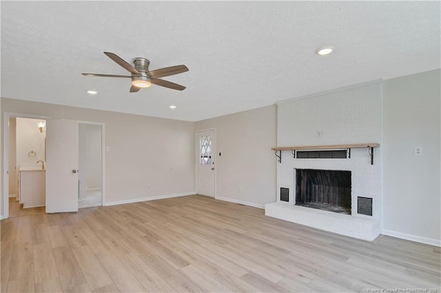 unfurnished living room with a textured ceiling, light wood-style flooring, a fireplace, and visible vents