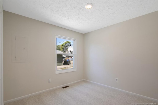 empty room with a textured ceiling, light carpet, visible vents, baseboards, and electric panel