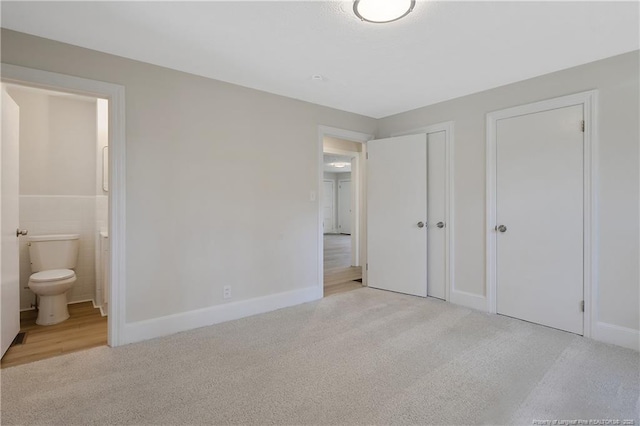 unfurnished bedroom featuring tile walls, carpet flooring, and ensuite bathroom