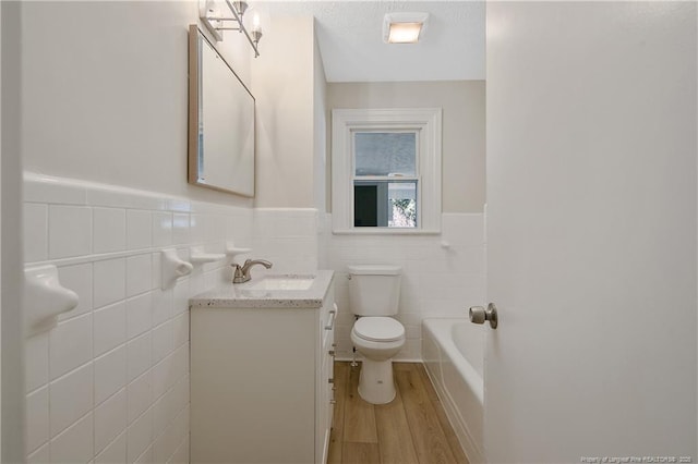 bathroom featuring a wainscoted wall, toilet, vanity, wood finished floors, and a tub