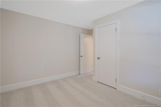 spare room with baseboards and light colored carpet