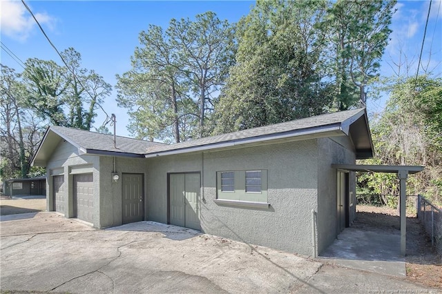 exterior space with roof with shingles, stucco siding, an attached garage, fence, and driveway