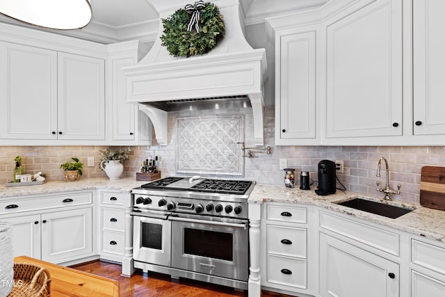 kitchen with premium range hood, white cabinetry, range with two ovens, and a sink