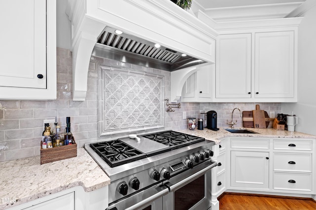 kitchen featuring white cabinets, custom range hood, range with two ovens, and a sink