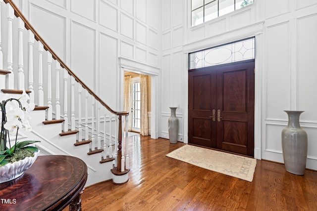 entryway featuring a decorative wall, stairway, a high ceiling, and wood finished floors