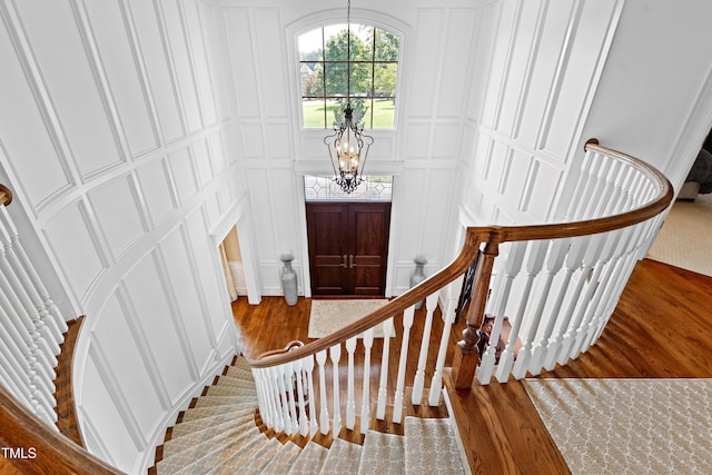 foyer with stairs, a notable chandelier, wood finished floors, and a decorative wall