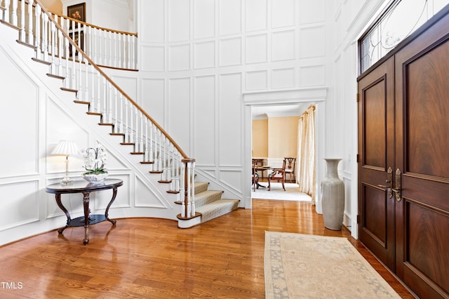 entryway featuring a decorative wall, stairway, a towering ceiling, and wood finished floors