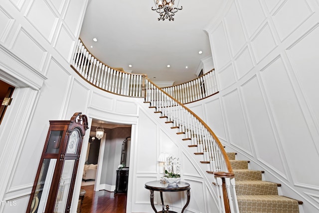 stairs featuring arched walkways, a decorative wall, a towering ceiling, an inviting chandelier, and wood finished floors