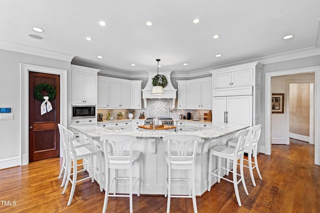 kitchen featuring white cabinets, decorative backsplash, a spacious island, custom range hood, and built in appliances