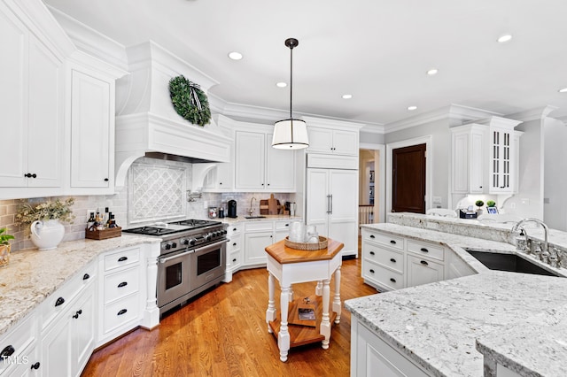 kitchen with high end appliances, light wood-style flooring, ornamental molding, white cabinetry, and a sink