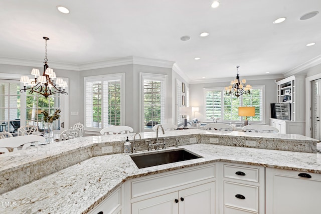 kitchen featuring a chandelier, a sink, white cabinetry, and light stone countertops