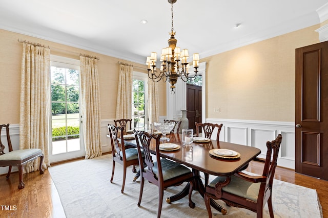 dining area featuring ornamental molding, light wood finished floors, a wainscoted wall, and an inviting chandelier