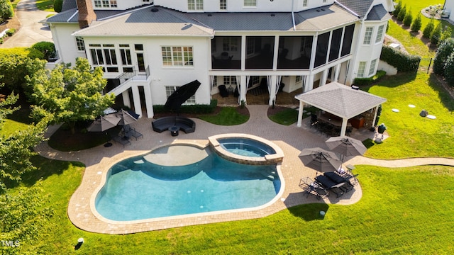 rear view of property featuring a patio, a lawn, a pool with connected hot tub, and a sunroom