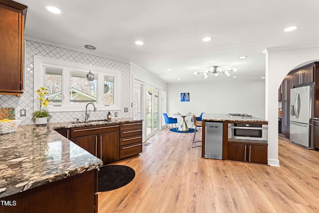 kitchen with arched walkways, light wood-style flooring, stone counters, stainless steel refrigerator with ice dispenser, and a sink