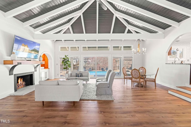 living room with beam ceiling, a notable chandelier, wood finished floors, a warm lit fireplace, and baseboards